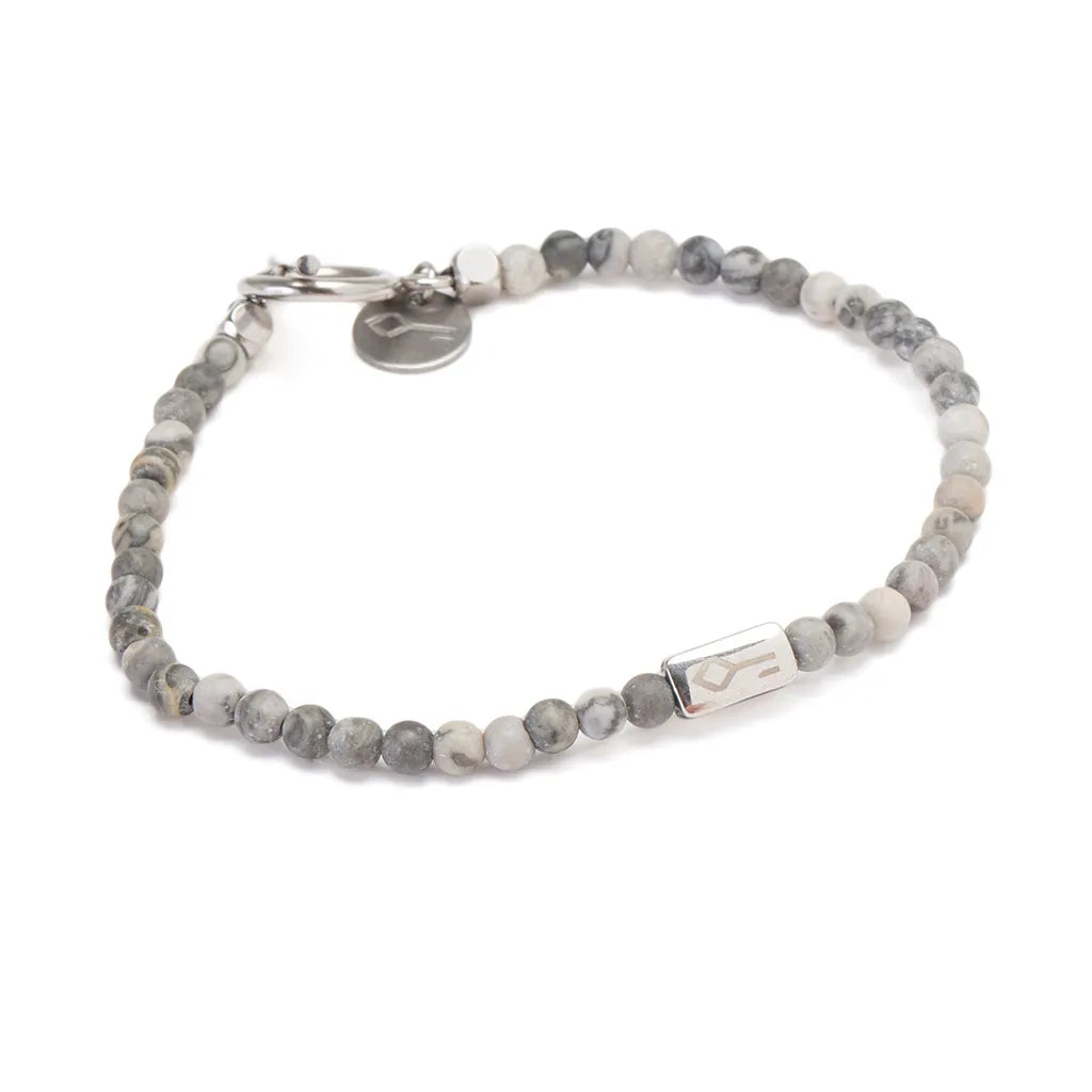 A delicate beaded bracelet featuring small round grey and white marbled stones, accented with a sleek rectangular stainless steel charm engraved with a minimalist logo. The bracelet is finished with a sturdy stainless steel clasp and an additional engraved charm, giving it a modern and refined look. Perfect for a subtle yet stylish accessory.