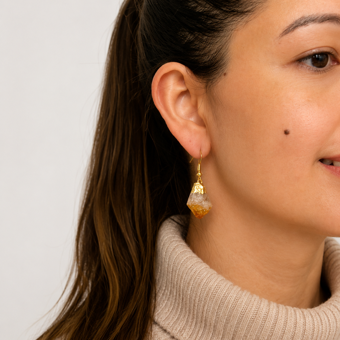Close-up of a person wearing a gold earring with a citrine gemstone against a neutral background
