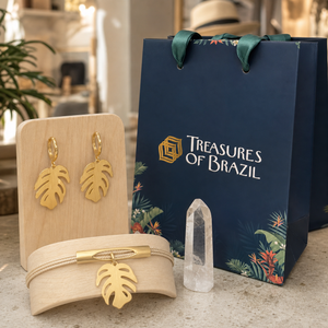 Monstera gold-coloured earrings and matching bracelet on wooden displays with crystal and Treasures of Brazil gift bag