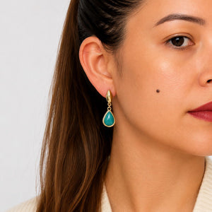 Close-up of a woman wearing a gold earring with a turquoise stone against a neutral background