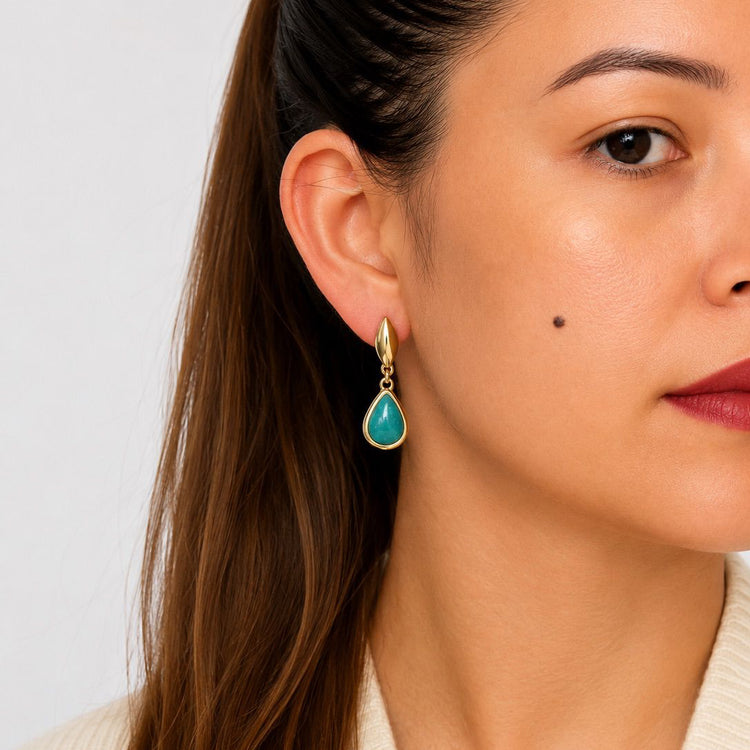 Close-up of a woman wearing a gold earring with a turquoise stone against a neutral background